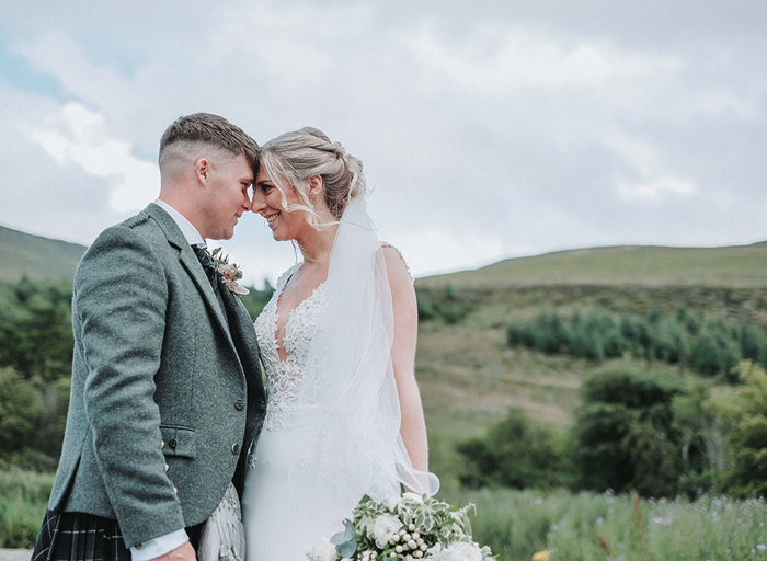 a happy bride and groom standing head to head with green hills and countryside in background