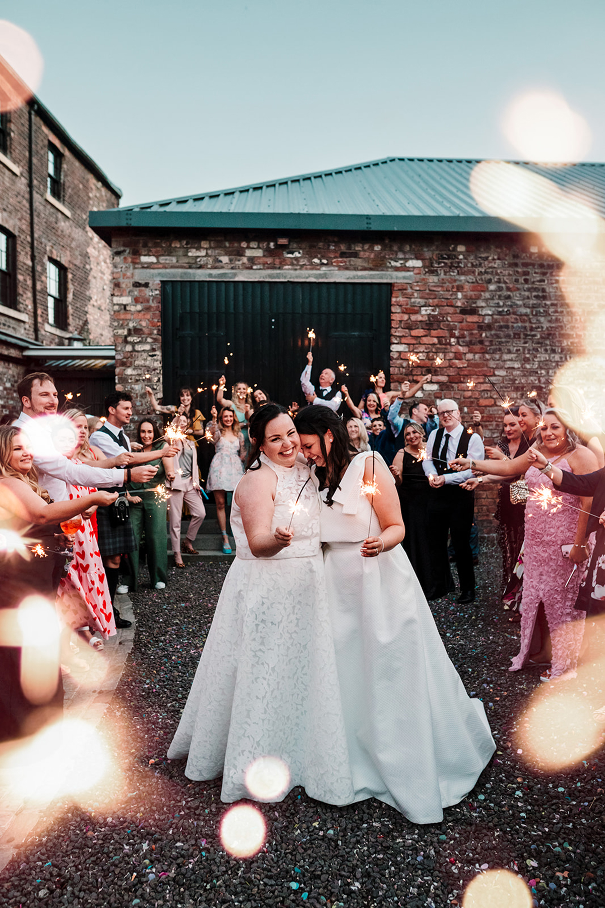 Two brides celebrate with guests holding sparklers outside The Engine Works wedding venue in Glasgow