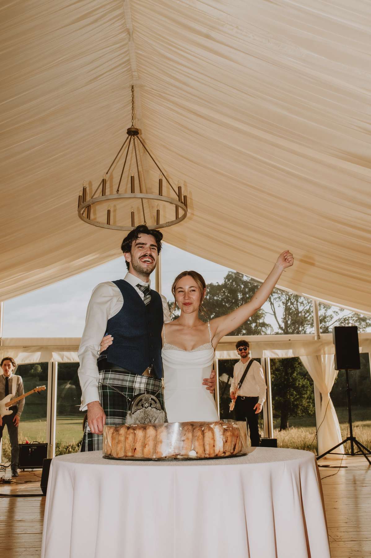 Newlyweds celebrate behind their wedding cake inside the marquee at Ballogie House