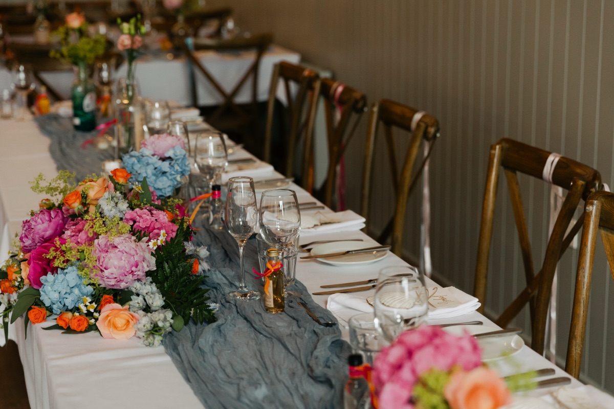 Colourful wedding table flowers in pink, orange and blue with a blue fabric runner at The Dougarie Boathouse on Arran.
