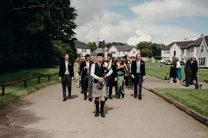 a group of people walking behind a man in a kilt playing the bagpipes