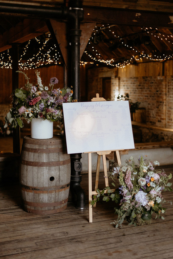 a wedding seating plan and large pink, purple and white flower displays in a rustic wooden barn setting at the Byre at Inchrya