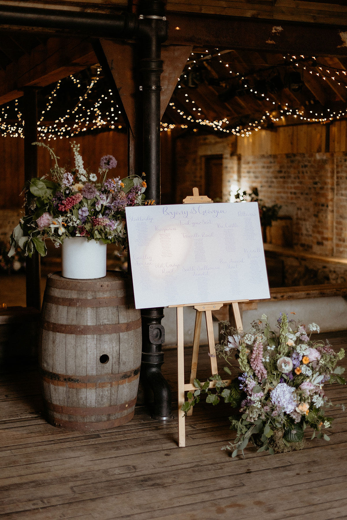 a wedding seating plan and large pink, purple and white flower displays in a rustic wooden barn setting at the Byre at Inchrya