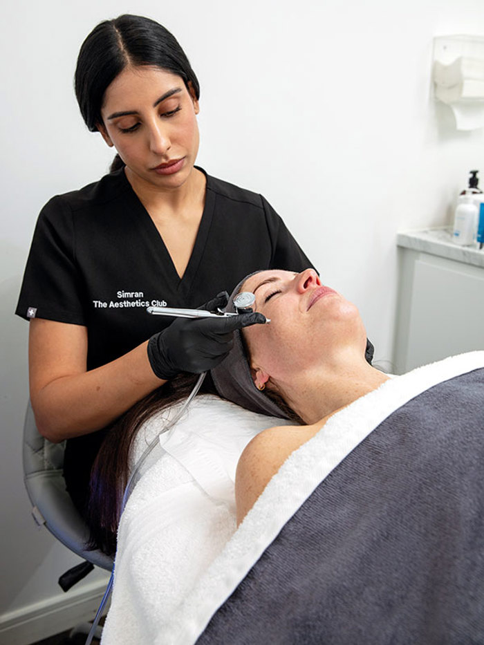 An aesthetics professional performs a facial to a client who is lying down