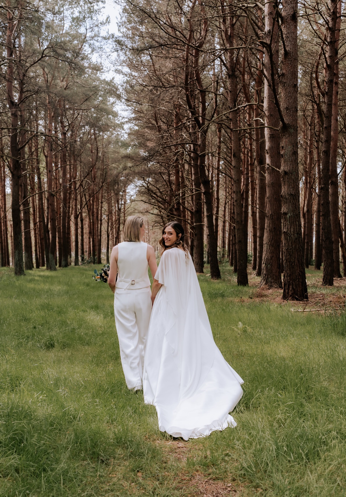 Hannah and Donna walking together through the woodland at Harvest Moon after their wedding ceremony.