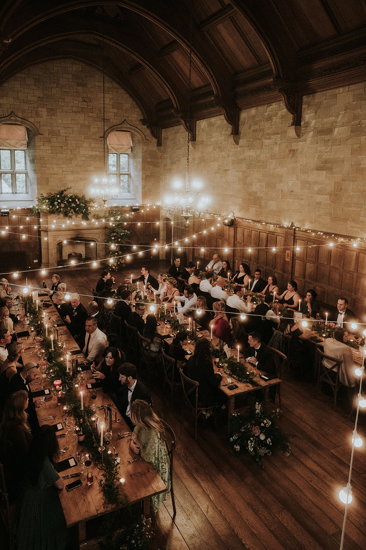 Wedding breakfast in Achnagairn Castle ballroom with long banquet tables, candlelit décor, festoon lighting and guests dining beneath the vaulted ceiling