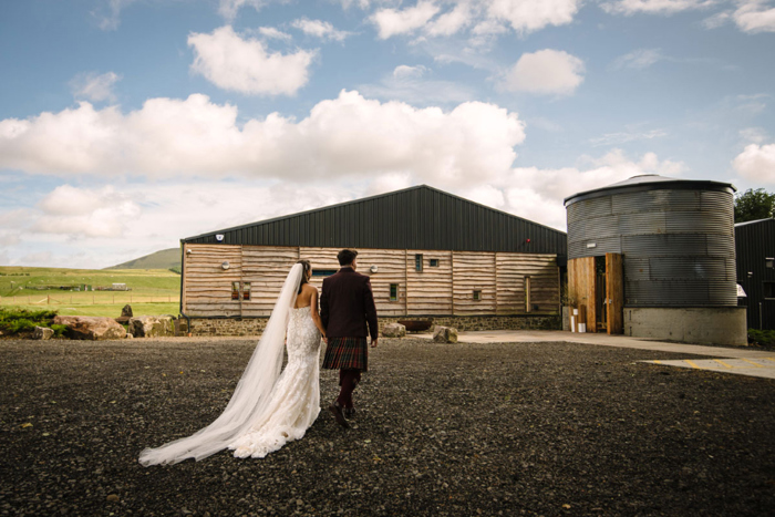 a bride and groom walking towards a barn
