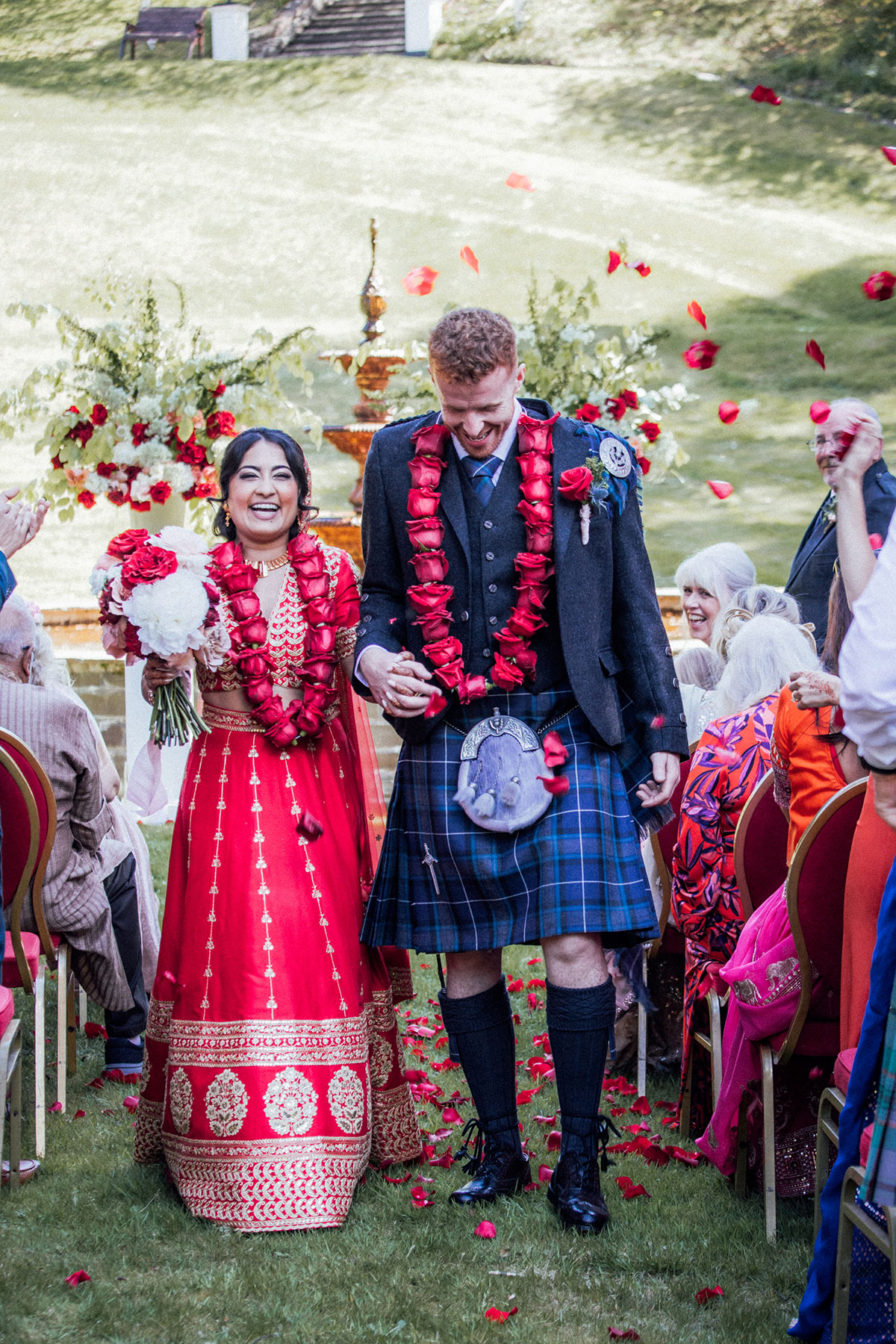 Bride and groom celebrating as they walk back up the aisle after their outdoor wedding ceremony with rose petal confetti