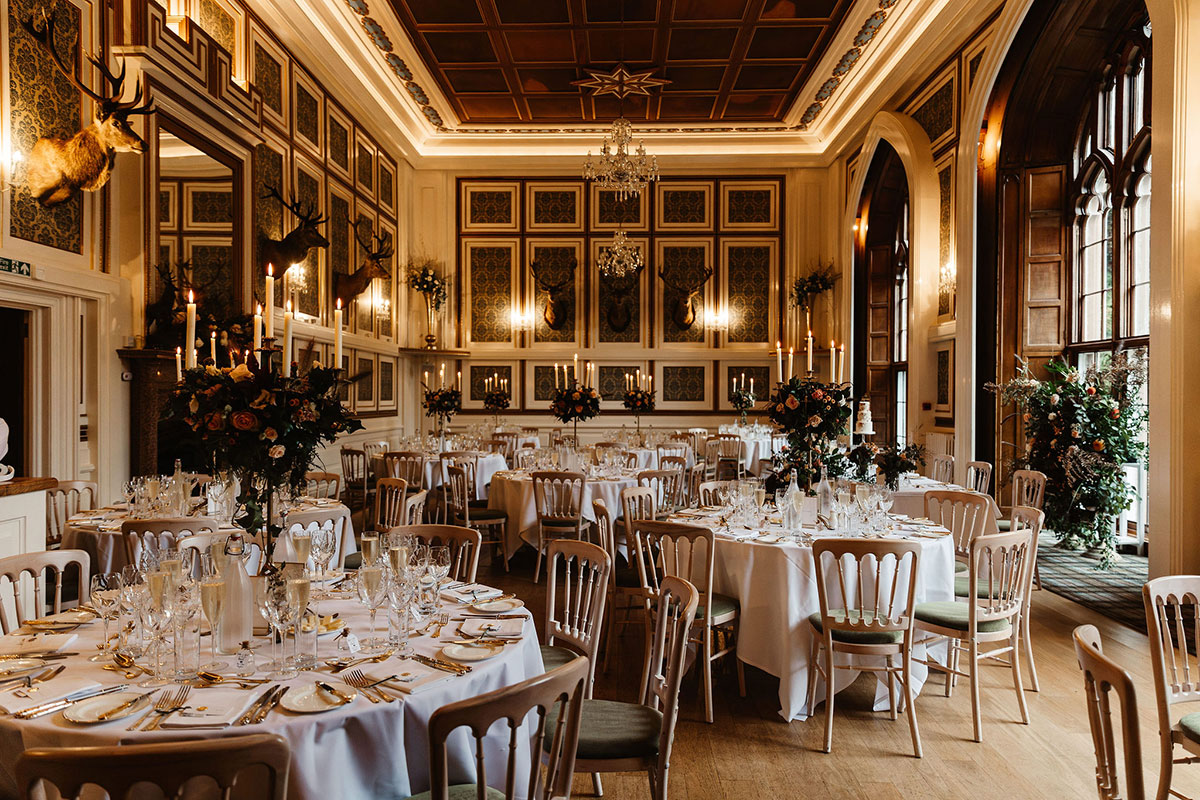 Grand dining room set for a wedding meal, with tall floral arrangements, chandeliers, and candlelit tables