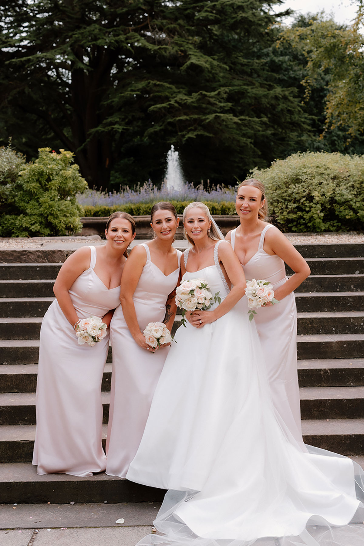 Bride and bridesmaids posing together on the steps at Mar Hall, holding soft pastel bouquets.