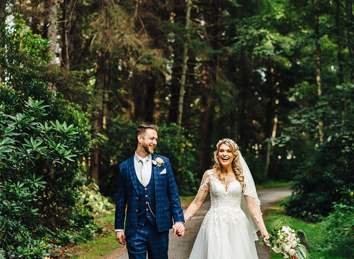 Newly-wed couple walk hand in hand down a forrest path