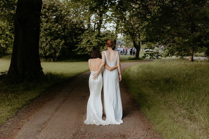 back of two brides walking along a path under trees at the Byre at Inchrya