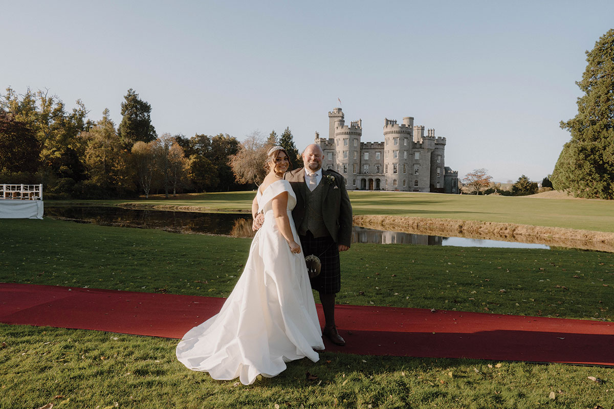Bride and groom posing outside Cluny Castle on a red carpet during their autumn Scottish castle wedding in Aberdeenshire.