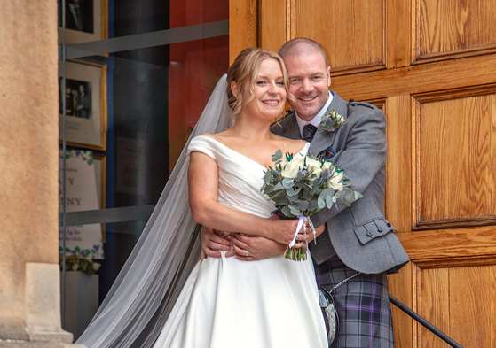 A bride and groom stand together in front of a large wooden door