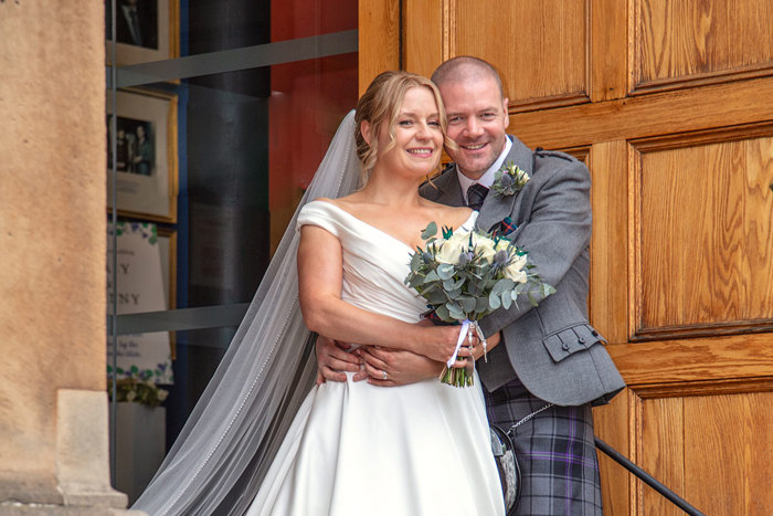 A bride and groom stand together in front of a large wooden door