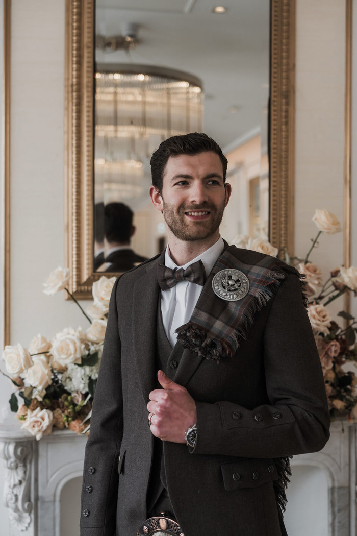 a smiling brown-haired groom wearing a brown tweed kilt jacket with fly plaid from MacGregor and MacDuff at the The Exchange in Glasgow