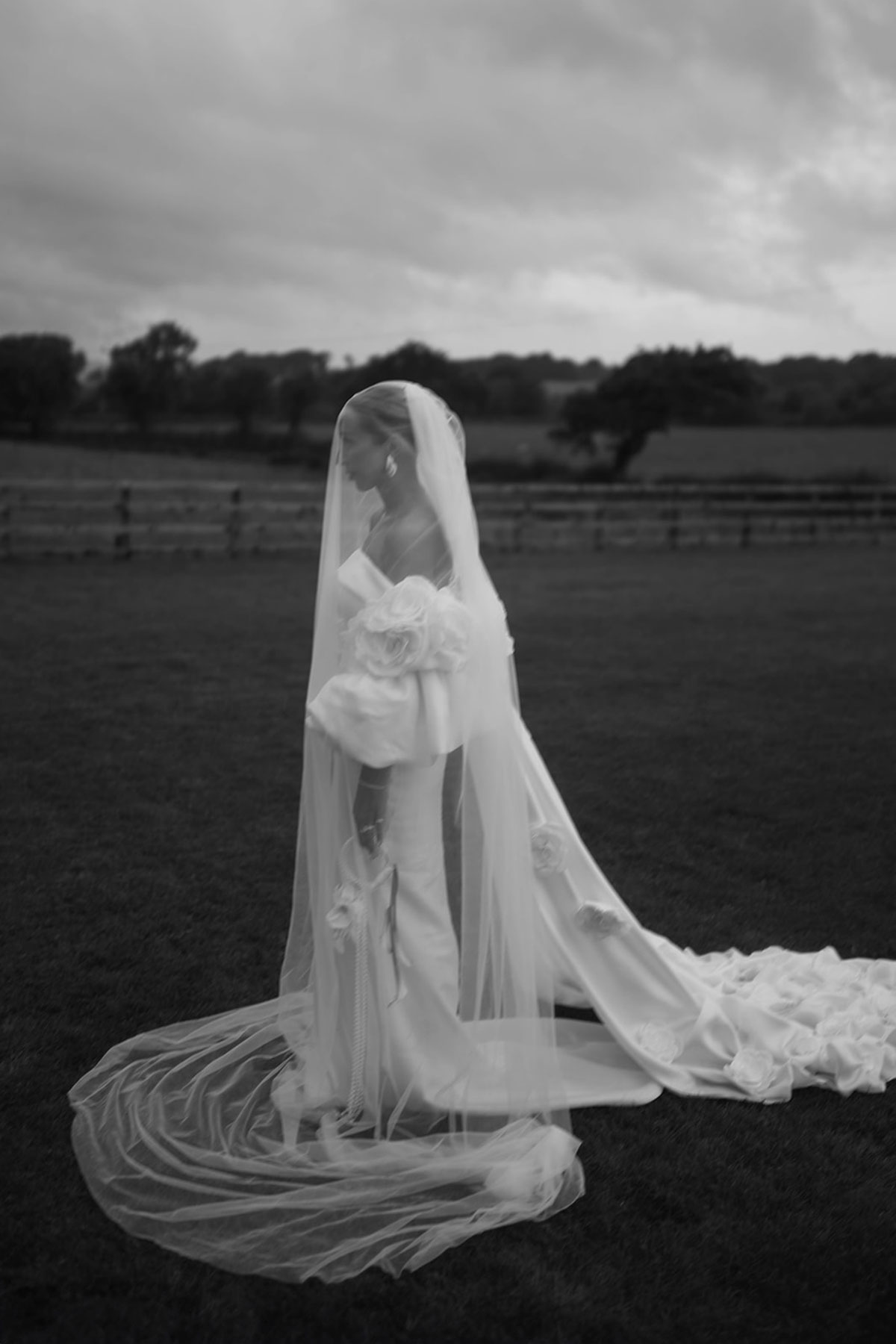 Black and white portrait of bride in long veil and off-the-shoulder wedding dress standing in an Ayrshire field.