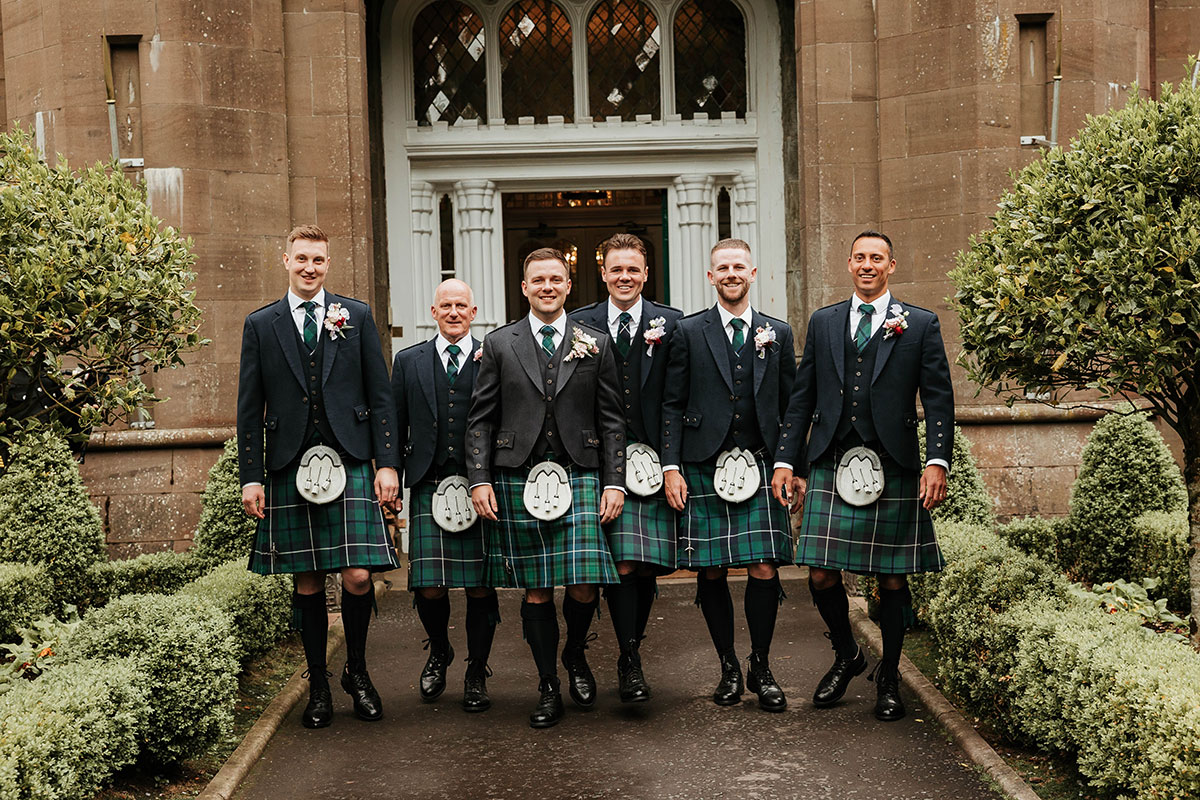 Groom and groomsmen in kilts walking outside Drumtochty Castle Aberdeenshire wedding venue