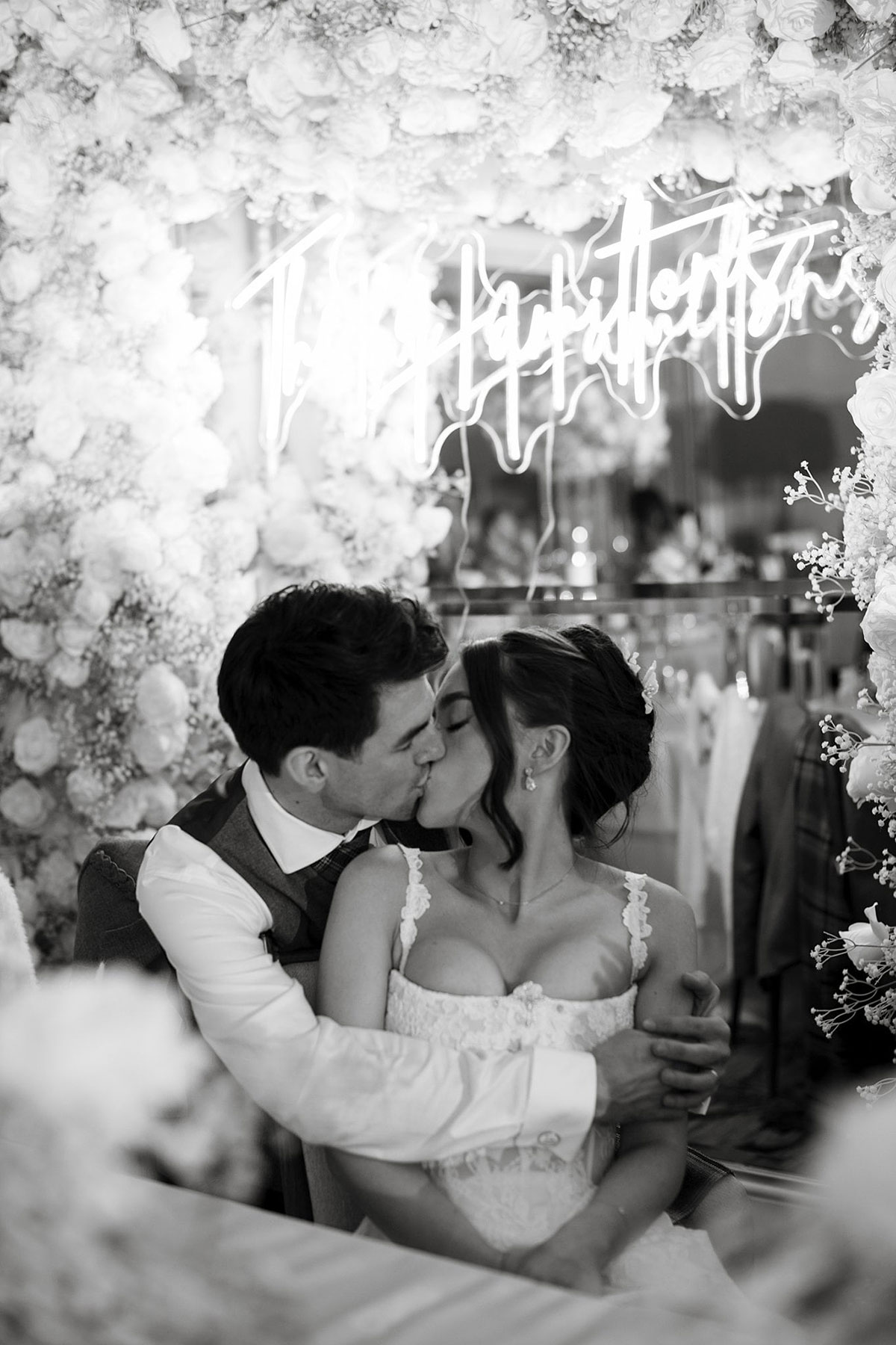 Bride and groom kissing beneath floral arch and neon sign during Old Course Hotel wedding reception in St Andrews.