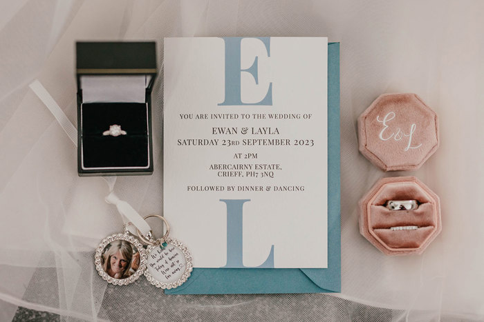 A wedding invitation, and two ring boxes with an engagement ring and wedding rings as well as a photo keyring