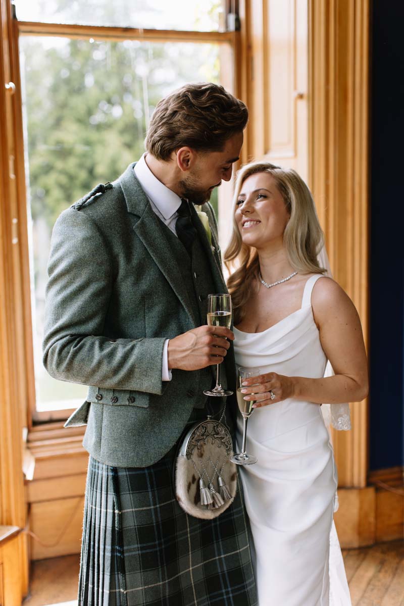 Lia and Louis enjoy glasses of champagne together inside Cambo House on their wedding day.
