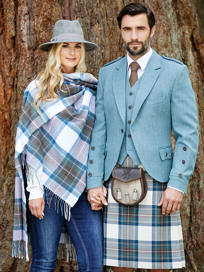 A woman in a blue hat and blue tartan shawl holding hands with a man in a blue and white kilt