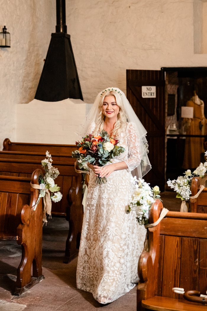 bride walks down the aisle at gretna green in lace dress holding orange bouquet 