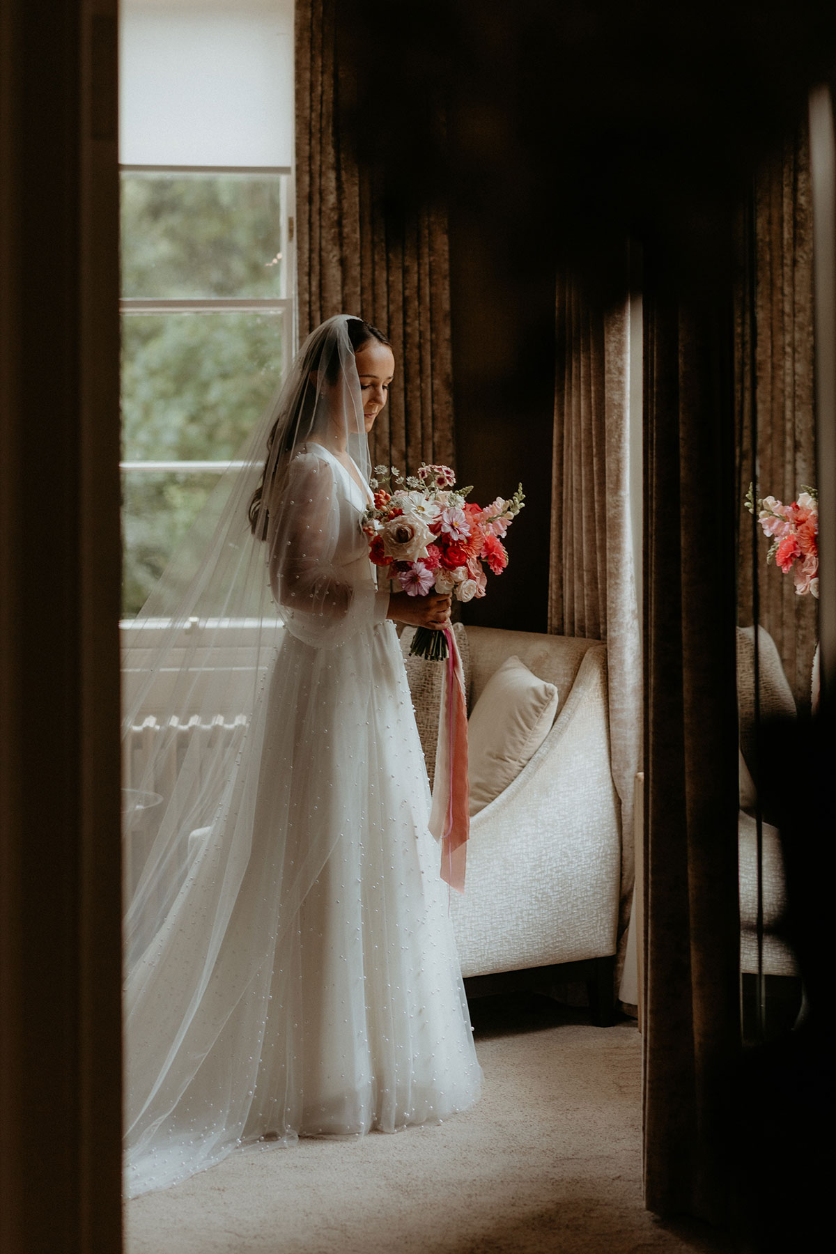 a bride in a doorway with a colourful bouquet by Gloam