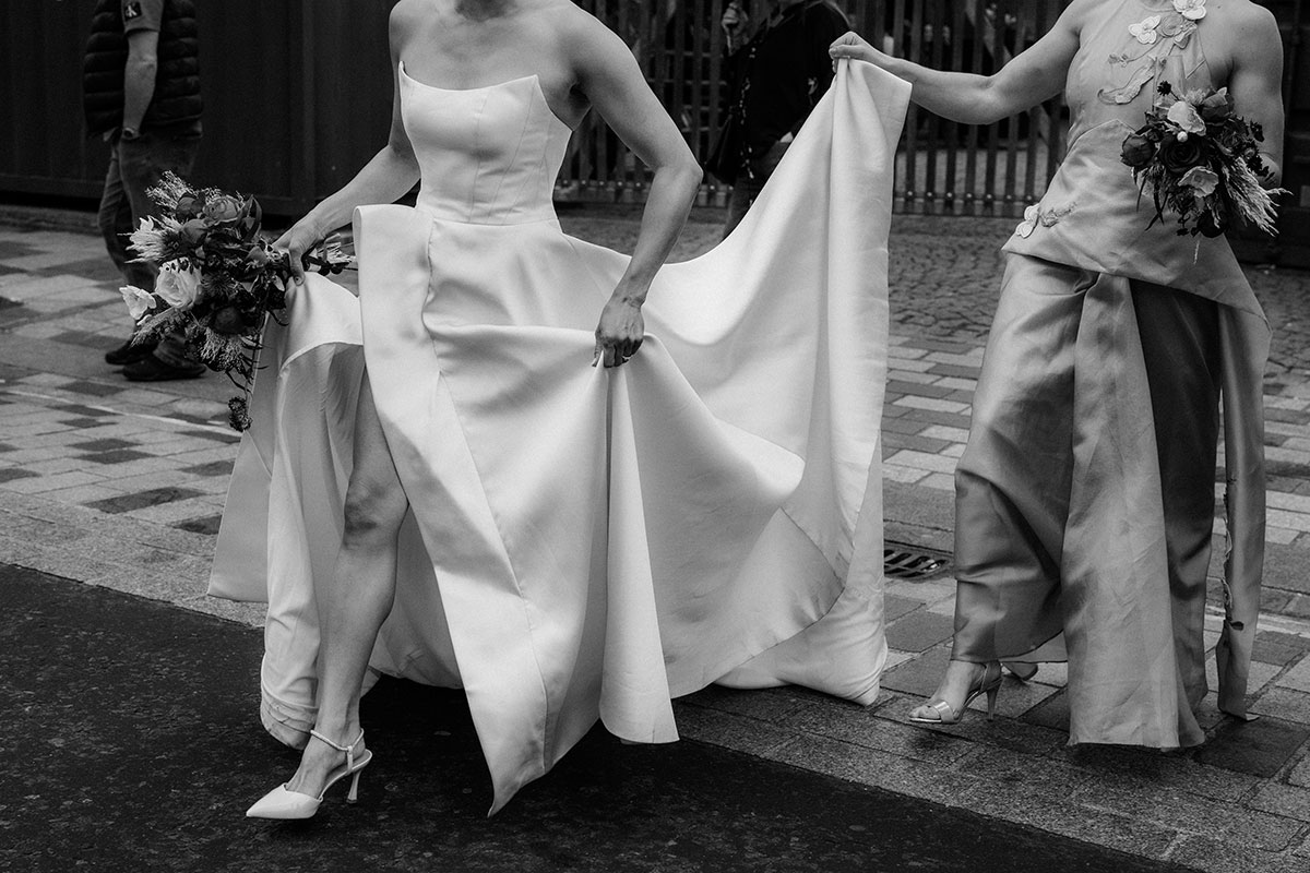 Bride lifting structured wedding dress while walking with bridesmaid on Glasgow street outside BAaD