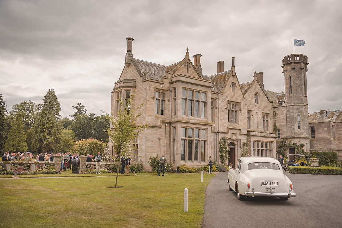 A white vintage car parked outside a country house