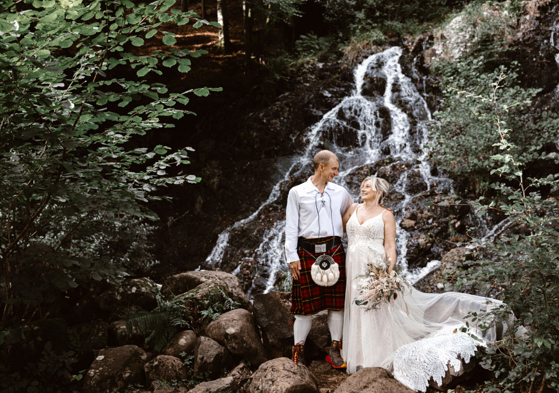 Bride and groom pose in front of a waterfall