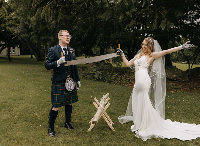 A bride and groom holding a two-person saw above a tree brand 