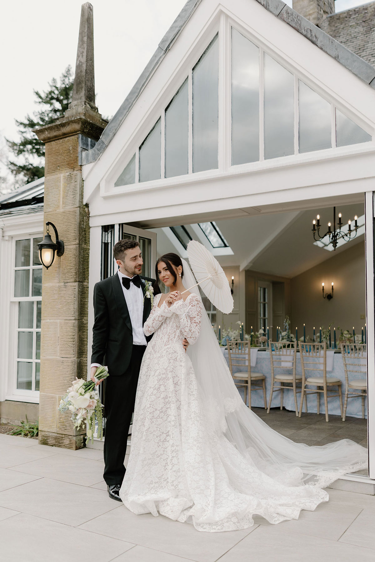 Bride and groom standing outside a conservatory entrance with a white parasol