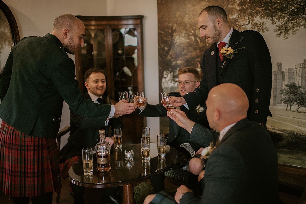 groom and groomsmen toasting with glasses of whisky at in drawing room at Achnagairn Castle