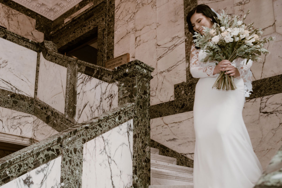 Bride walks down marble staircase holding her bouquet