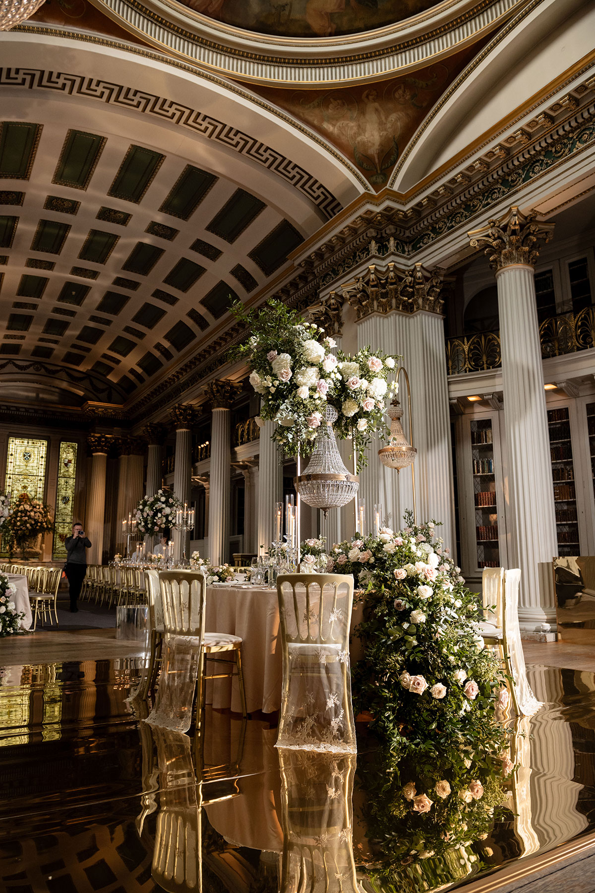 Luxurious wedding reception setup inside a grand hall with tall columns, ornate ceilings and elaborate floral arrangements with hanging chandeliers