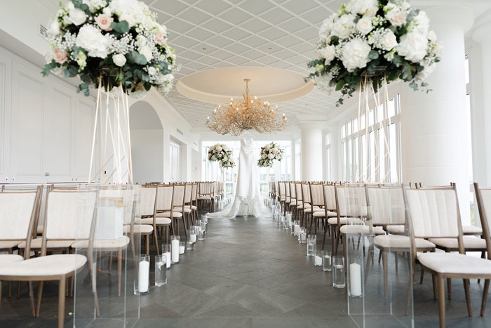 the Conservatory at the Old Course Hotel set for a wedding ceremony with tall round floral arrangements on perspex plinths and rows of cream chairs.