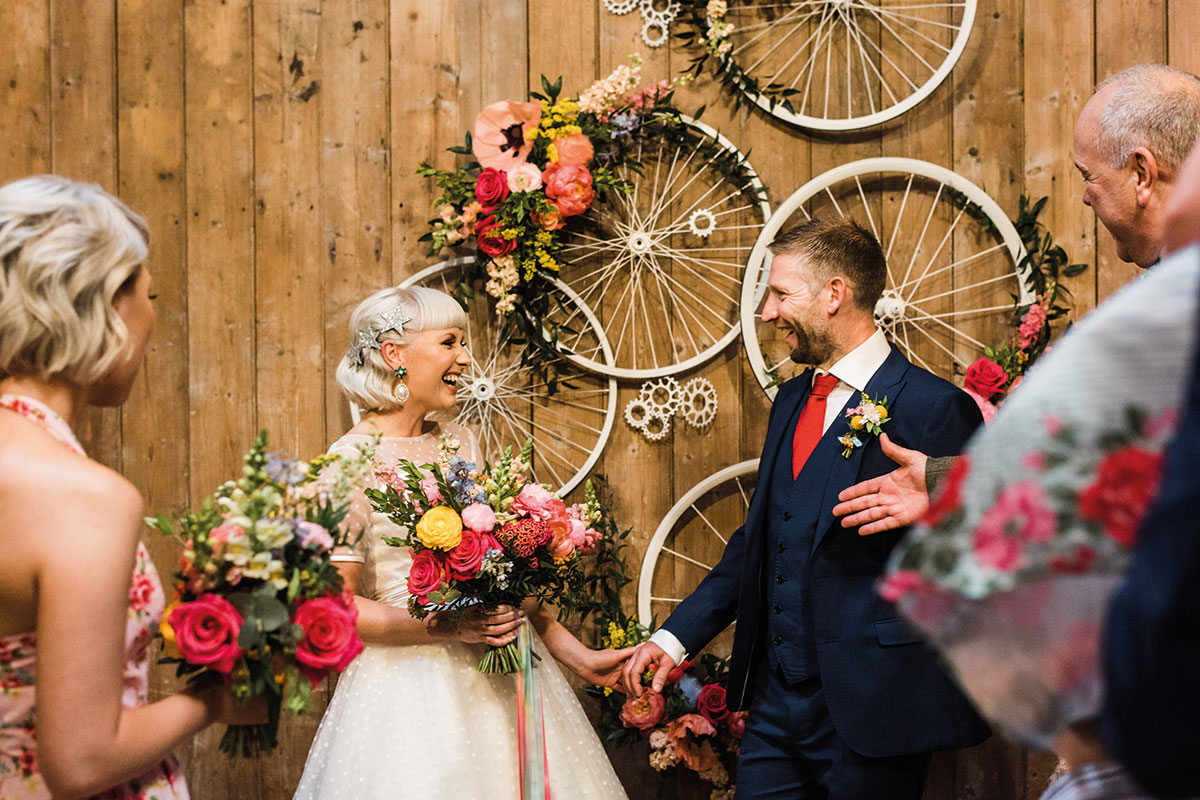 bride and groom get married with colourful flowers and bicycle wheels behind them