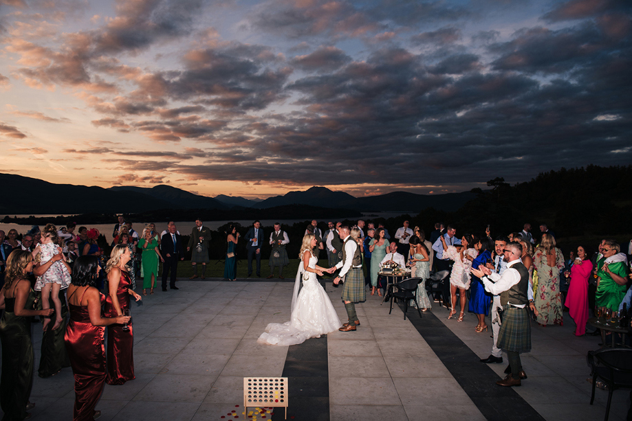 Bride and groom dance on outdoor dancefloor with guests around them