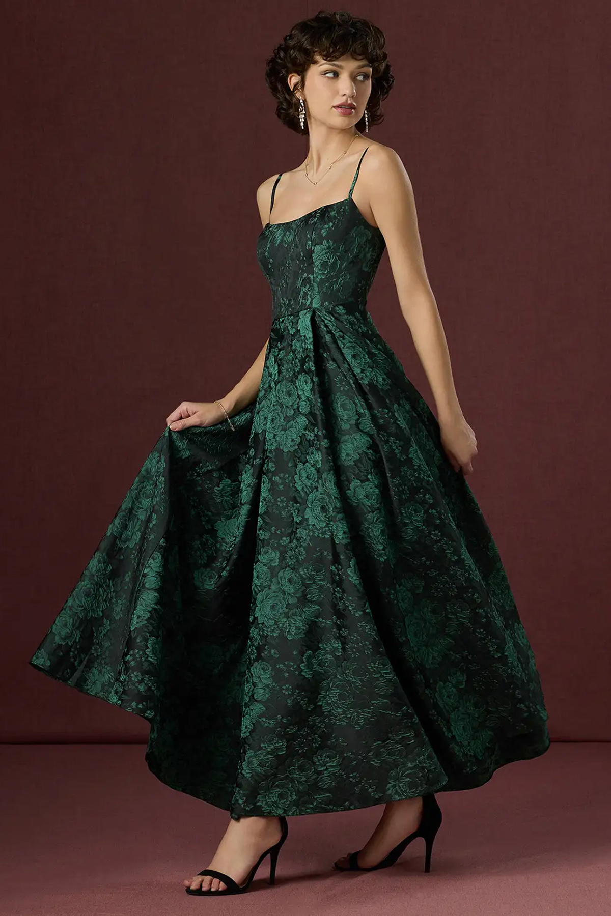 Model wearing an emerald-green and black floral jacquard maxi dress with thin straps and a full skirt.