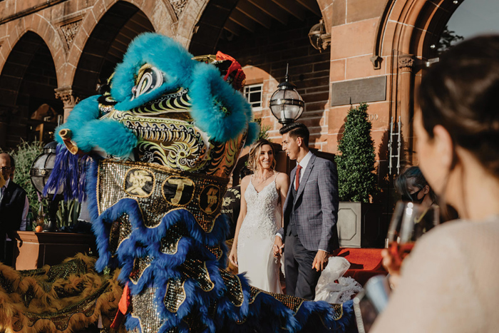 a bride and groom stand next to a blue Chinese dragon