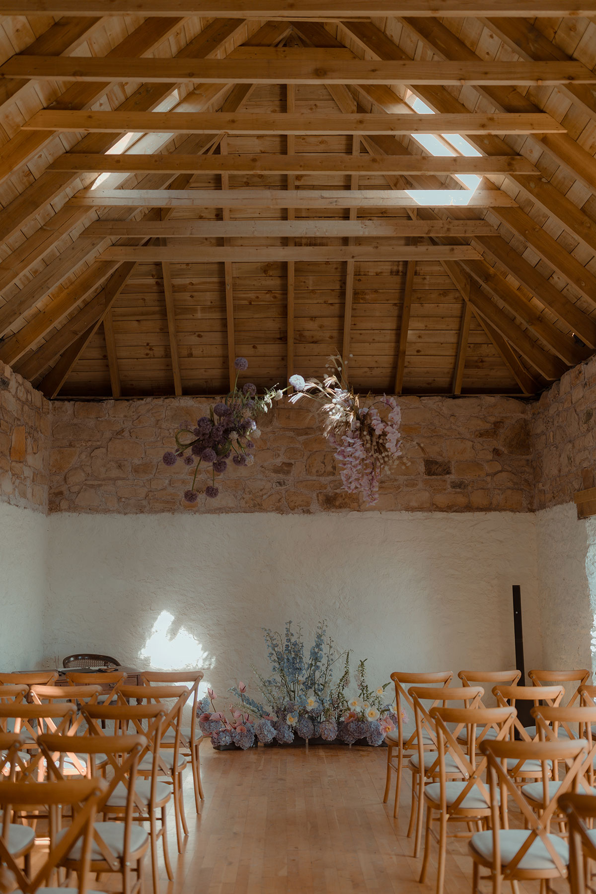Rustic barn wedding ceremony at a Falkirk farm venue with wooden chairs, exposed beams and hanging floral installations
