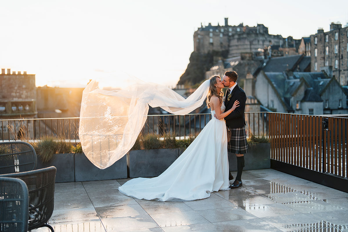 bride and groom kiss on wedding day at Virgin Hotels Edinburgh with edinburgh castle in the background