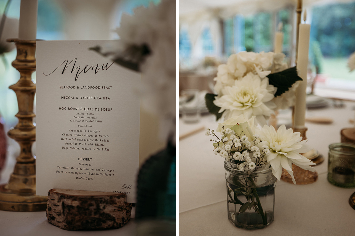 A Wedding Menu Propped On A Cut Log On Left And White Flowers In A Jam Jar On A Table On Left