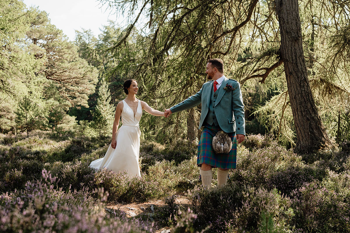 Bride and groom walking hand in hand through woodland and heather during wedding portraits in the Scottish Highlands