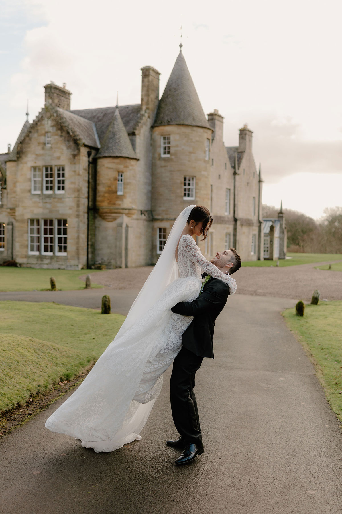 Groom lifting bride outside a historic stone estate building
