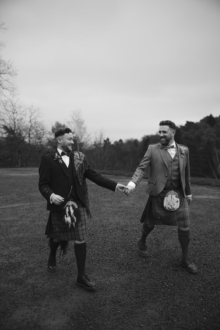 two grooms walking hand in hand outside Neidpath Castle
