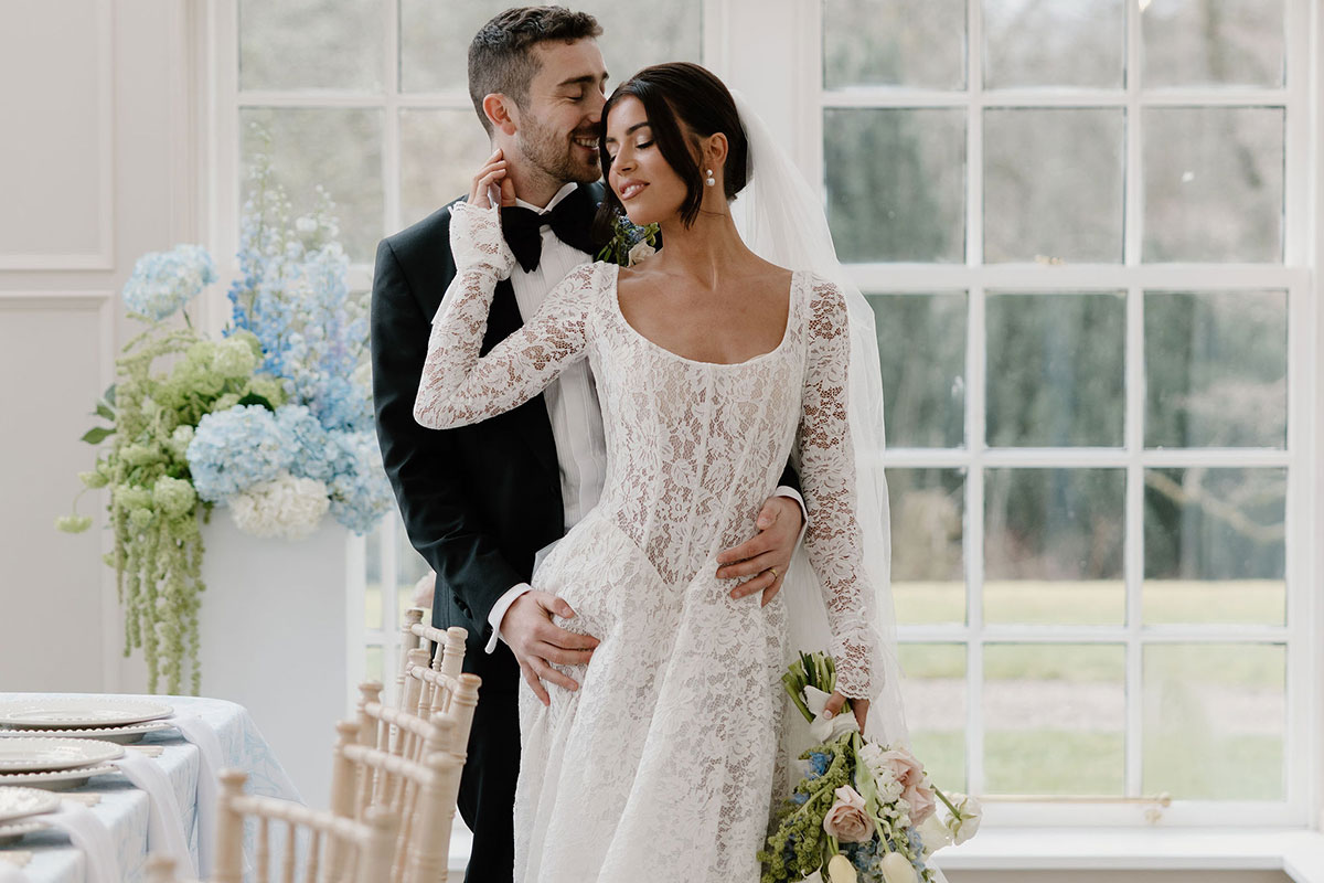 Bride and groom embracing beside large conservatory windows