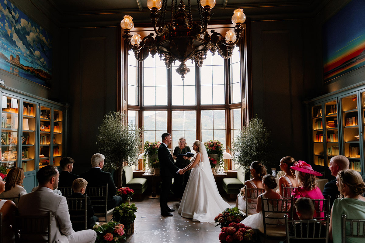 Bride and groom exchanging vows in front of large bay windows with scenic views during their Mar Hall ceremony.
