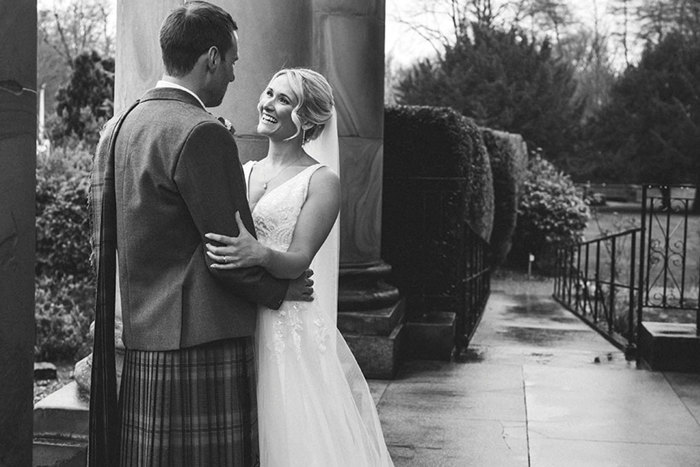 black and white photo of smiling bride and groom stood outdoors 